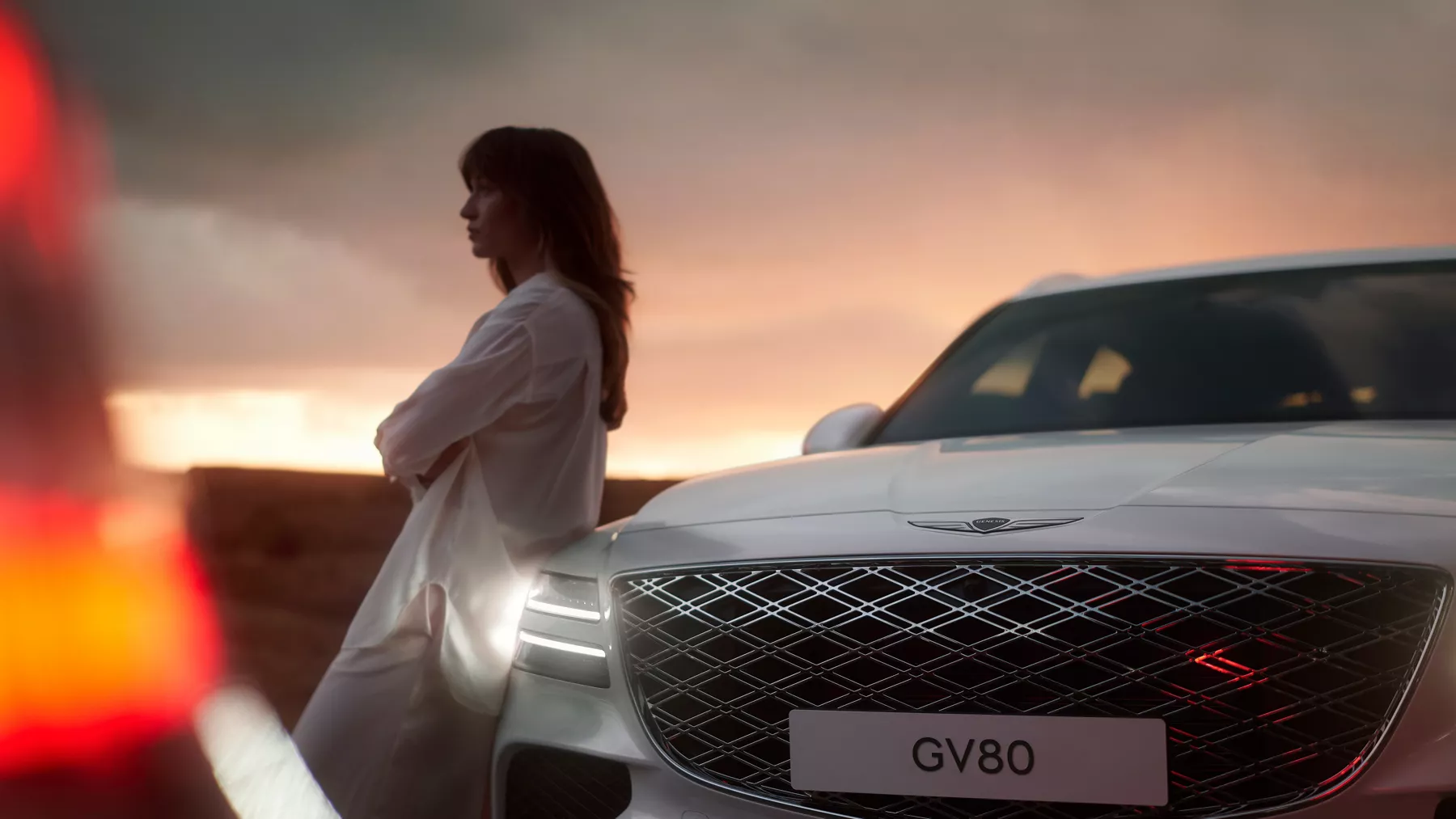 Front grille of GV80 with a woman leaning against the vehicle hood.