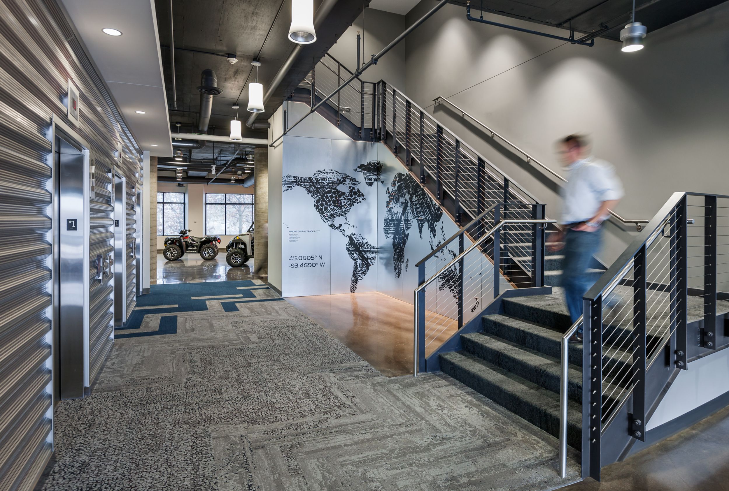 Interface HN810, HN820, HN840 and HN850 plank carpet tiles in open stairwell with four wheelers in background at Polaris Industries image number 6