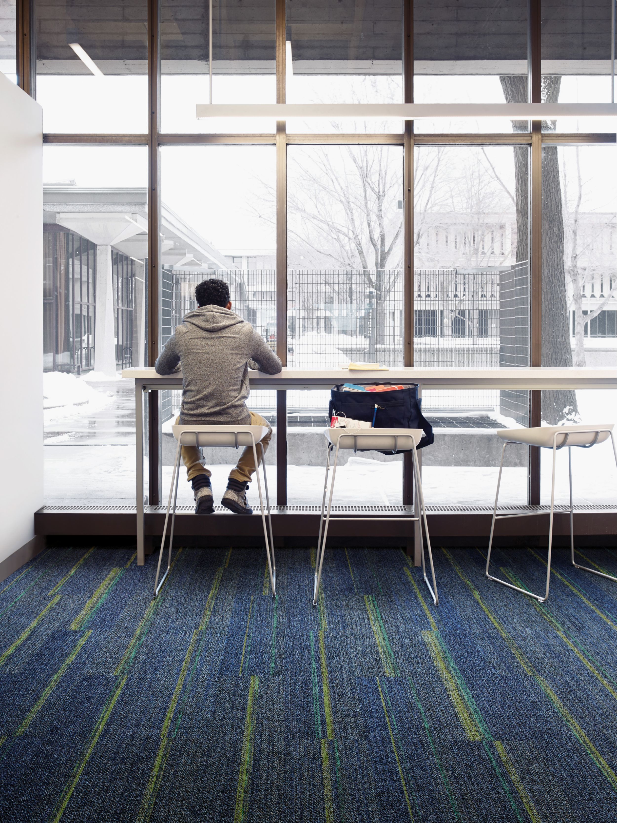 Interface Ground Waves plank carpet tiles in open area with student seated on stool image number 11