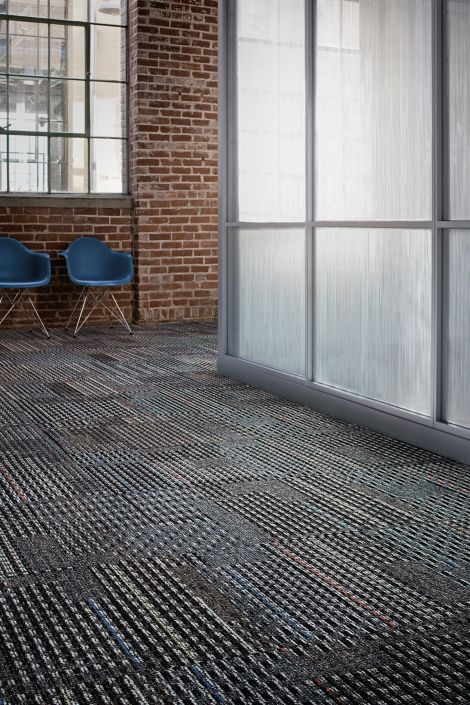 Interface Cotswold II carpet tile in open space and corridor with two blue chairs and exposed brick wall