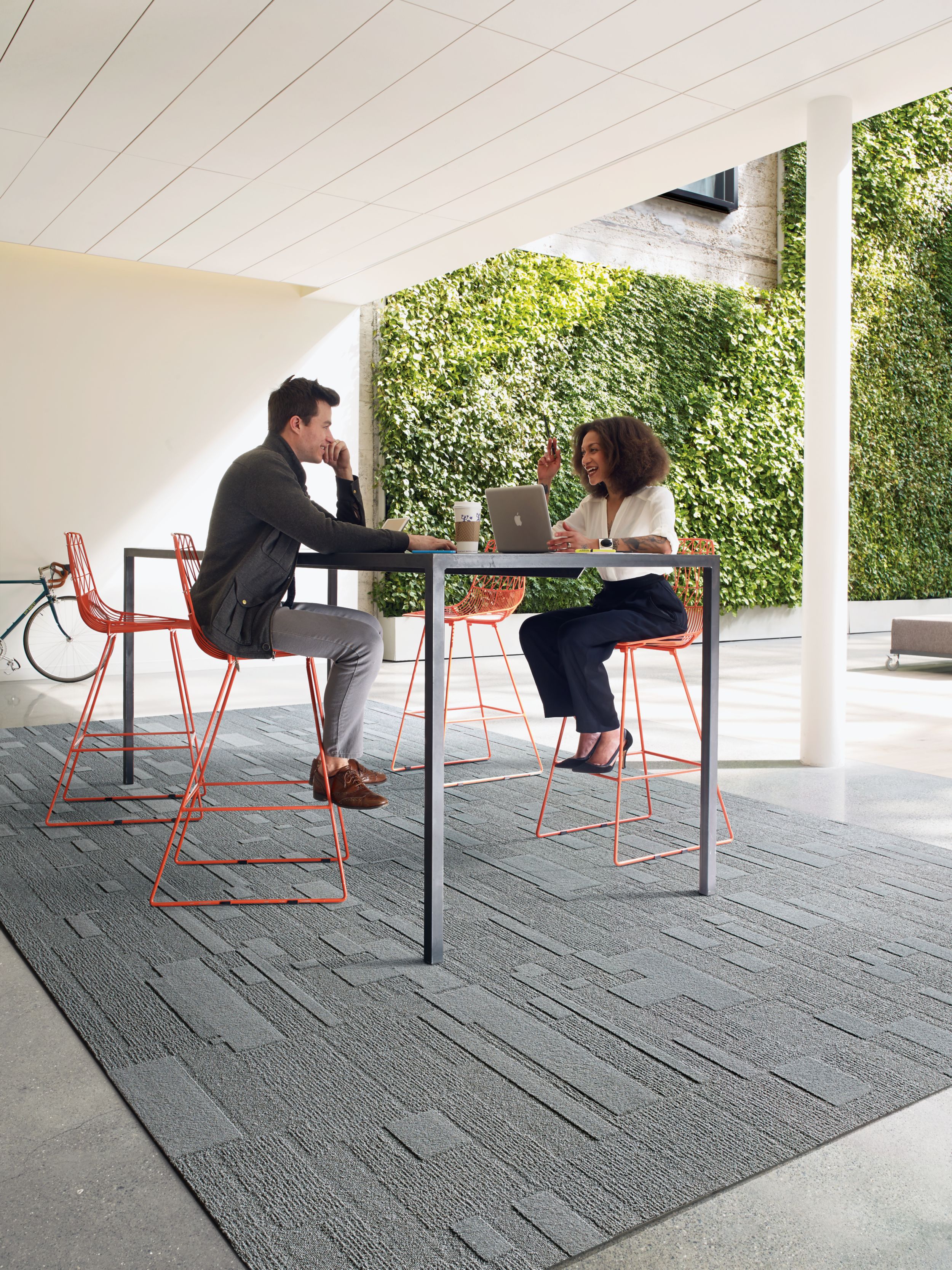 Interface EM552 plank carpet tile in covered outdoor space with vine wall in the background and man and woman meeting image number 5