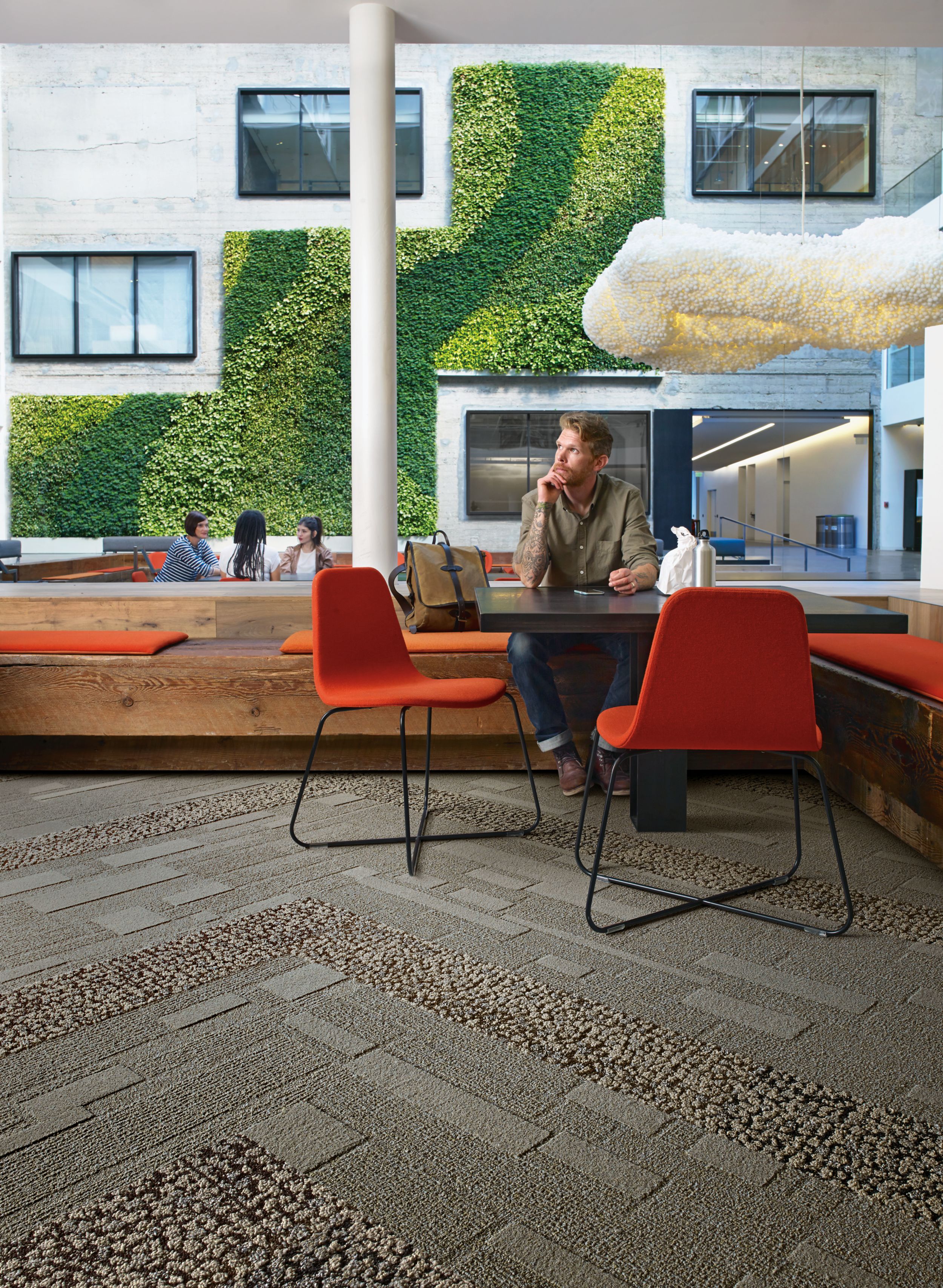Interface EM552 plank carpet tile with man sitting at table with lunch and group meeting in front of vine wall in the background  afbeeldingnummer 3