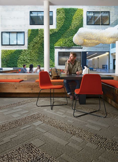 Interface EM552 plank carpet tile with man sitting at table with lunch and group meeting in front of vine wall in the background 