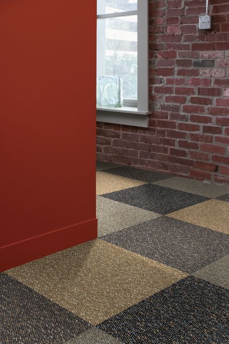 Interface Earth II carpet tile in corner with red wall and brick wall