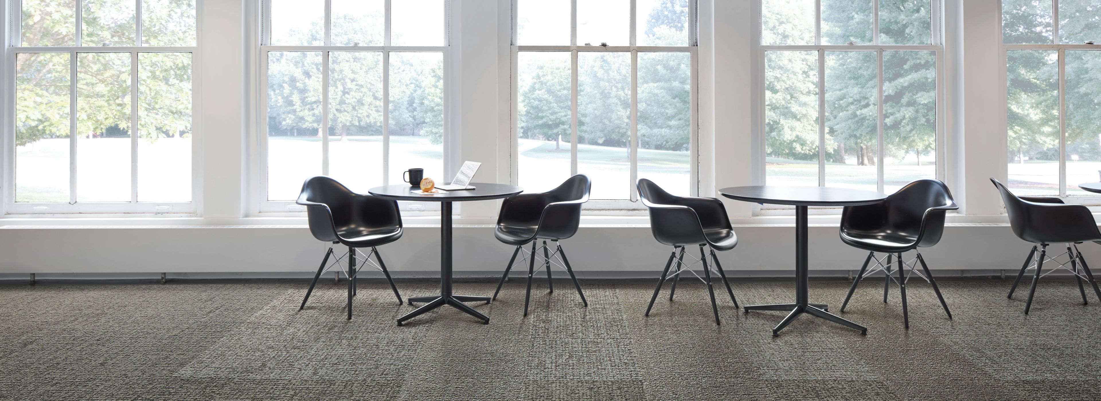 Interface Gridlock carpet tile with small tables against a wall of windows image number 1
