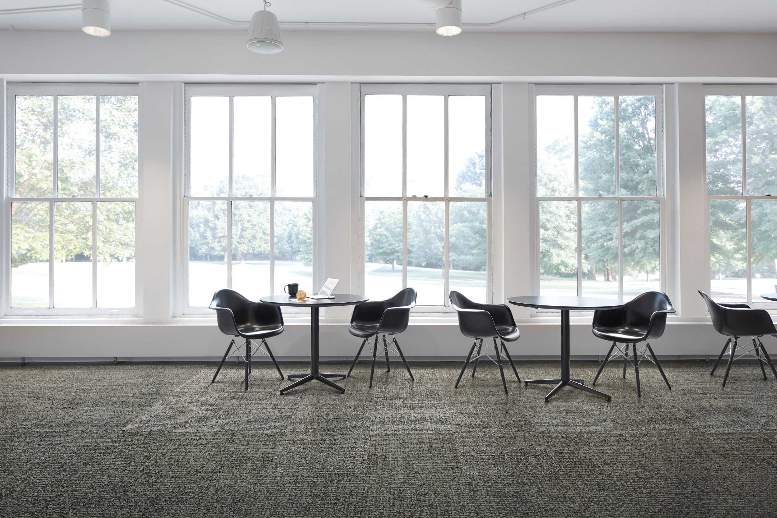 Interface Gridlock carpet tile with small tables against a wall of windows image number 1