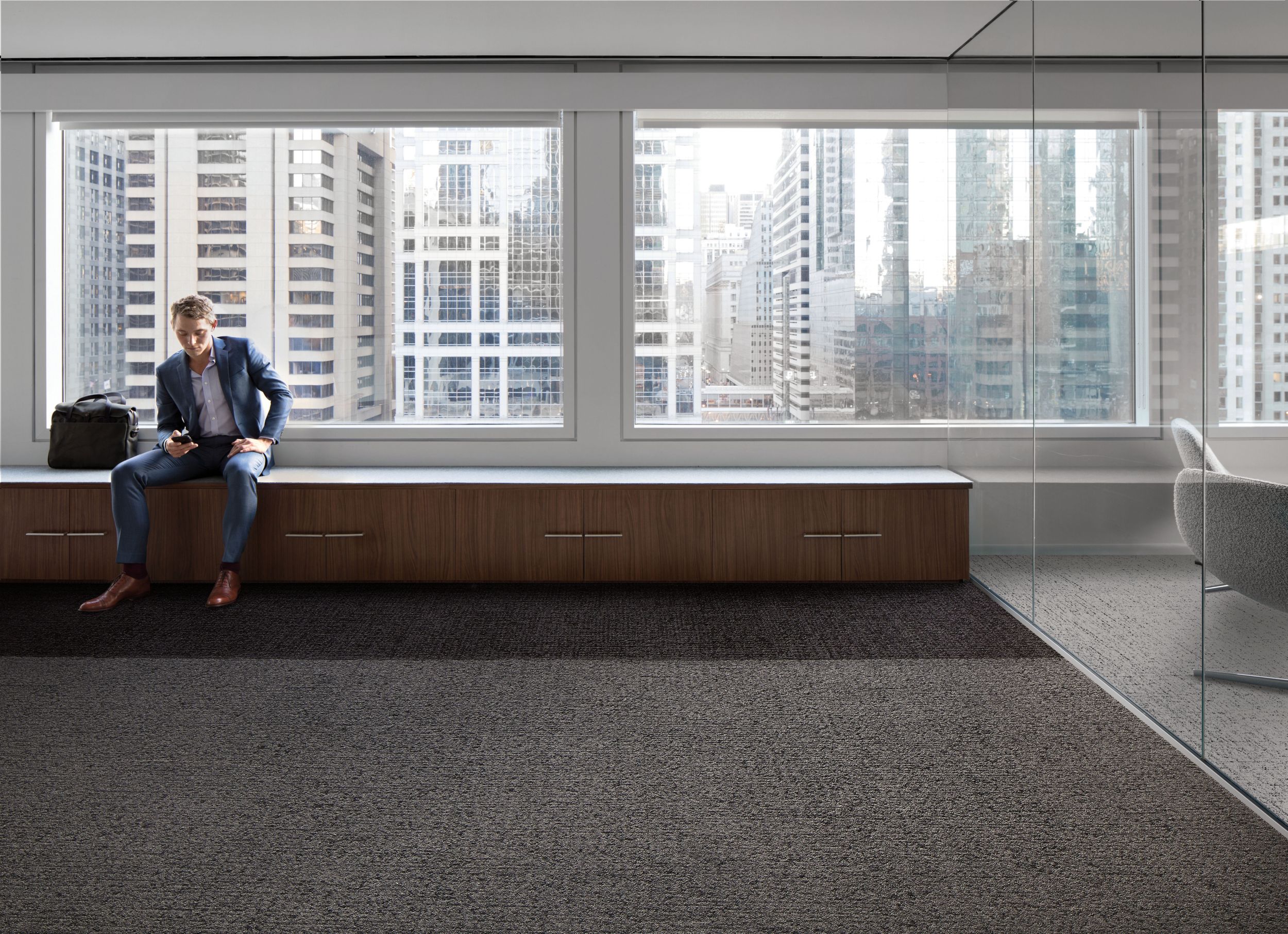Interface Gridlock and Riverwalk carpet tile with man sitting on long bench against windows of high-rise building imagen número 6