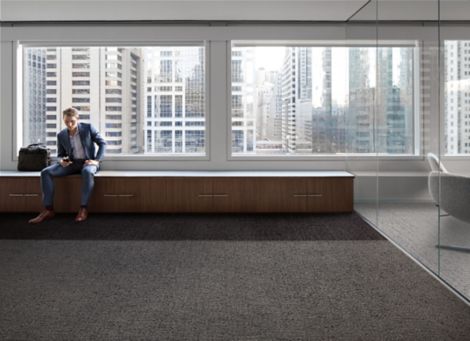 Interface Gridlock and Riverwalk carpet tile with man sitting on long bench against windows of high-rise building