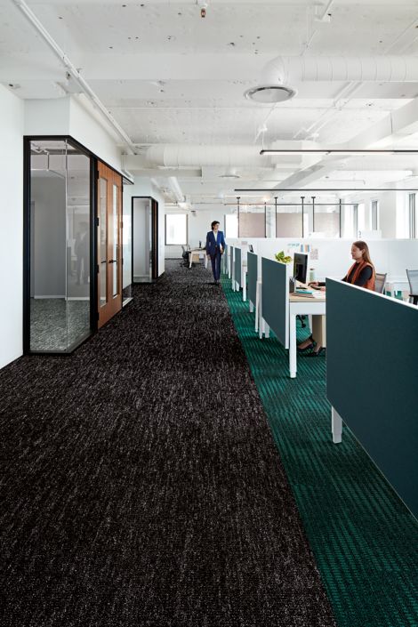 Interface Heart Strings carpet tile in long walkway between workspaces and meeting rooms with woman working at desk image number 2