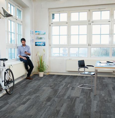 Interface Naturally Weathered plank carpet tile in office space with man looking at phone on window sill