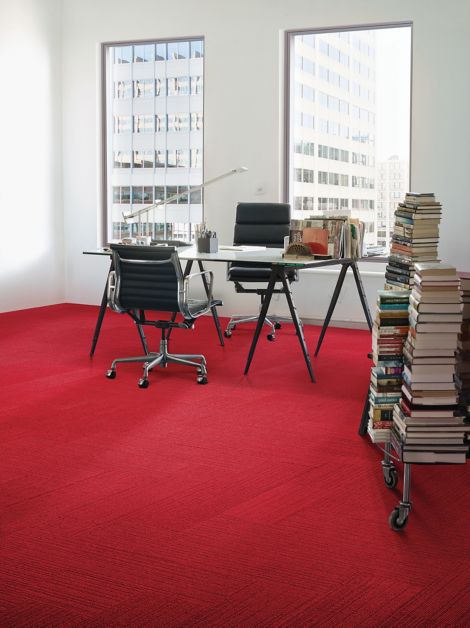 Interface On Line plank carpet tile in red in corner space with desk and stacks of books against wall