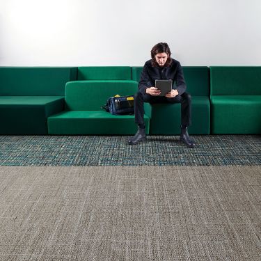 Interface Open Air 401 plank carpet tile with man working on tablet sitting on long green couch image number 1