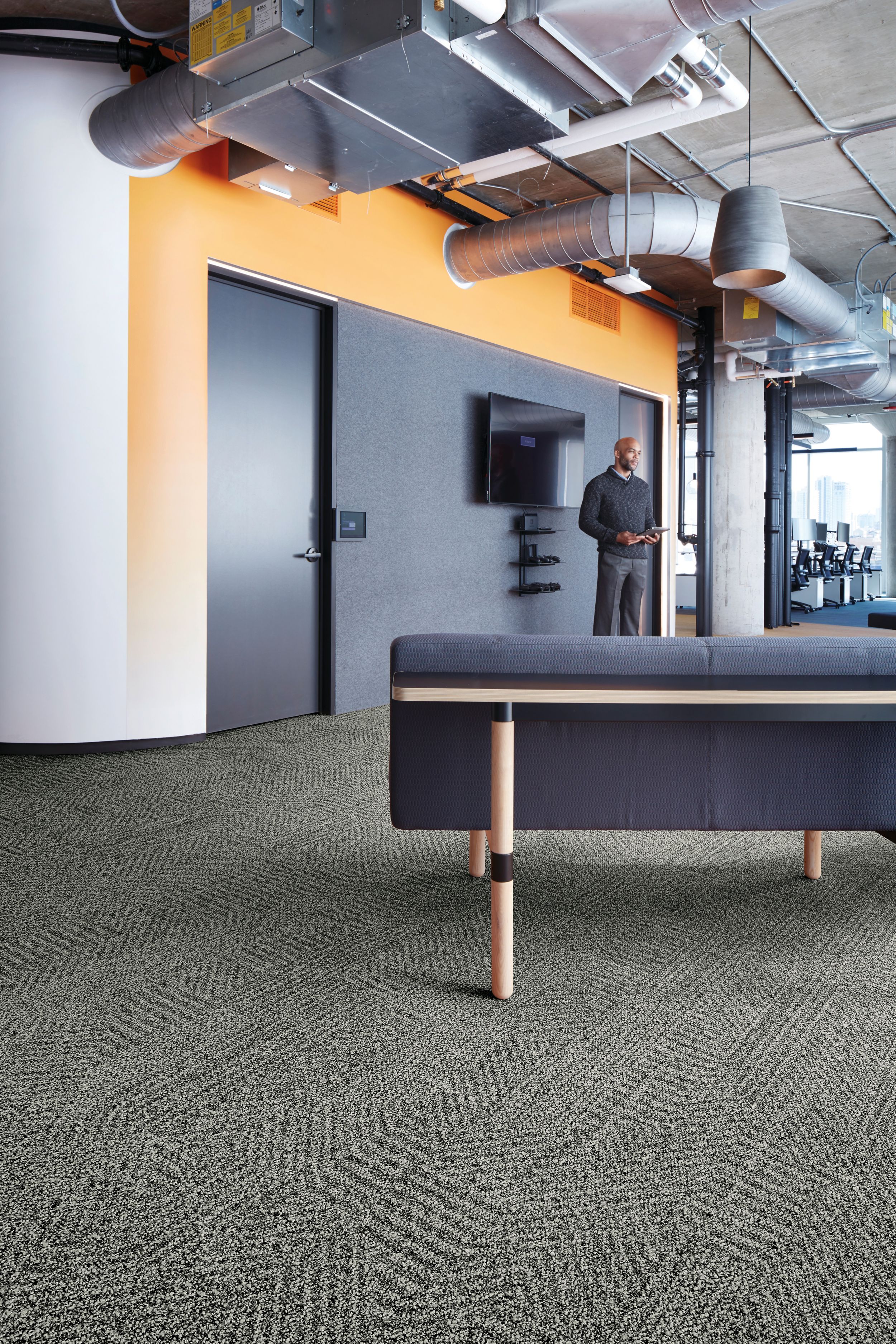 Interface Open Air 407 plank carpet tile with grey fabric couch and man standing in the background imagen número 1