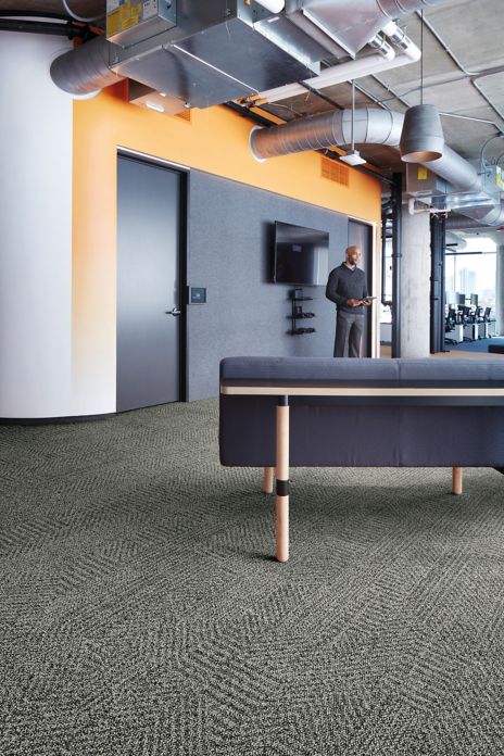 Interface Open Air 407 plank carpet tile with grey fabric couch and man standing in the background