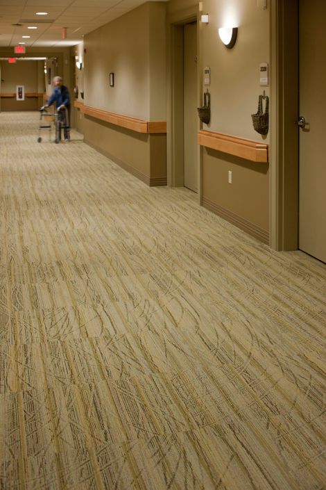 Interface Prairie Grass carpet tile in healthcare corridor with woman pushing man in wheelchair
