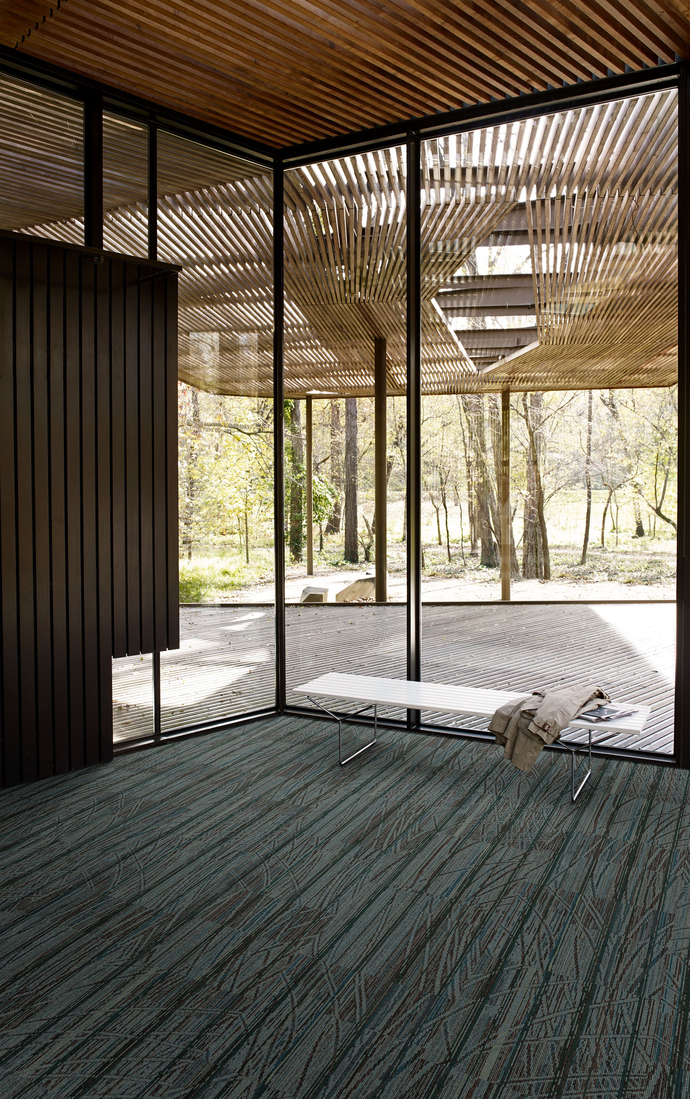 Interface Prairie Grass carpet tile in glass-enclosed room with white bench image number 1
