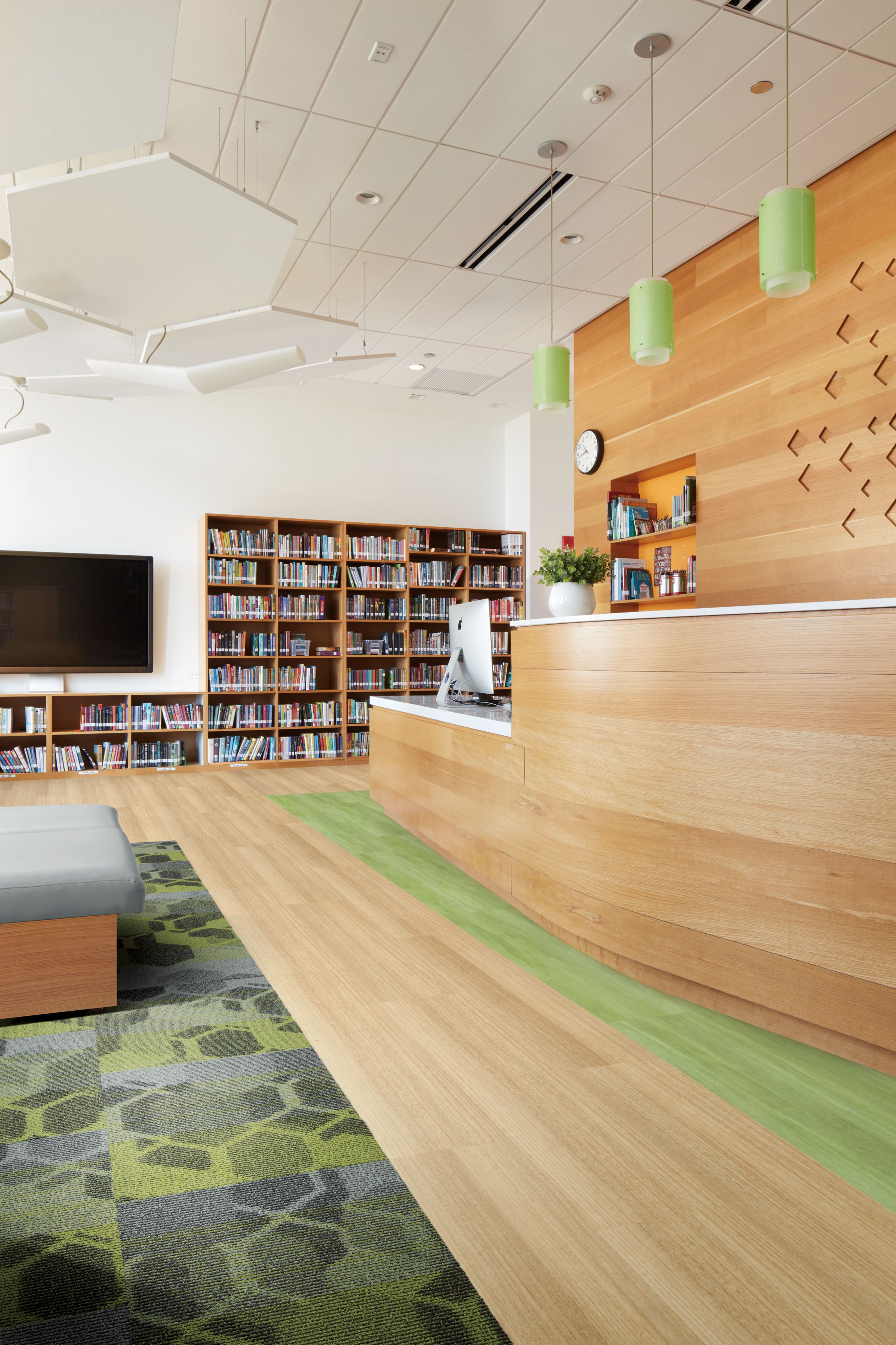 Interface Textured Woodgrains and Studio Set LVT with Honey Don't carpet tile in a common area with tv, desk and book shelves image number 4