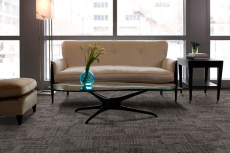 Interface Syncopation carpet tile in seating area with sofa, chair, wood side table and coffee table with blue glass vase