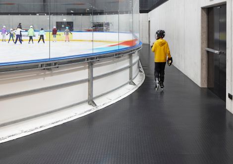 Child running with ice skates on a pastilled floor alongside an ice rink image number 3