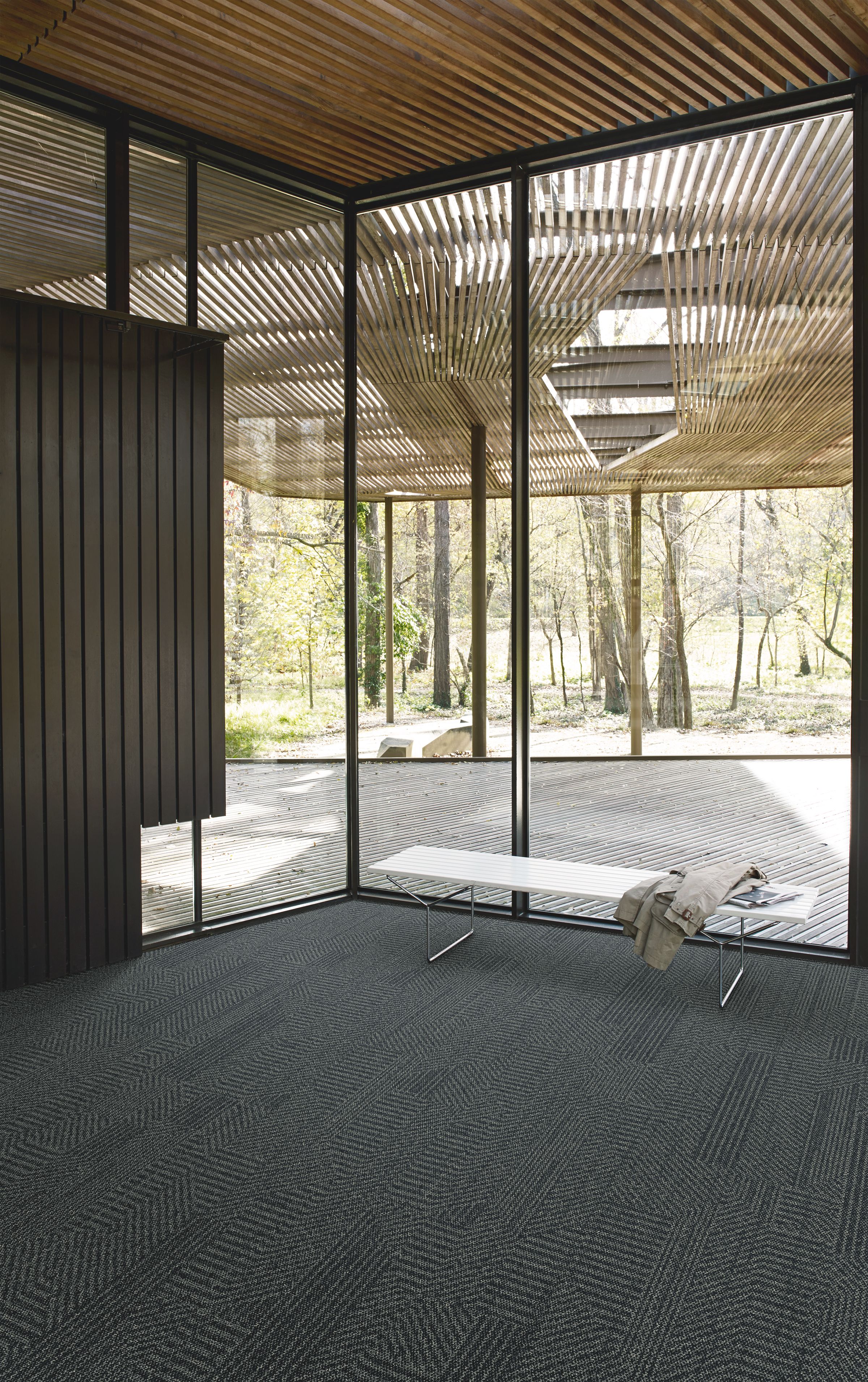 Interface Open Air 407 plank carpet tile in corner space with jacket draped over small white bench and wood slat ceiling imagen número 9