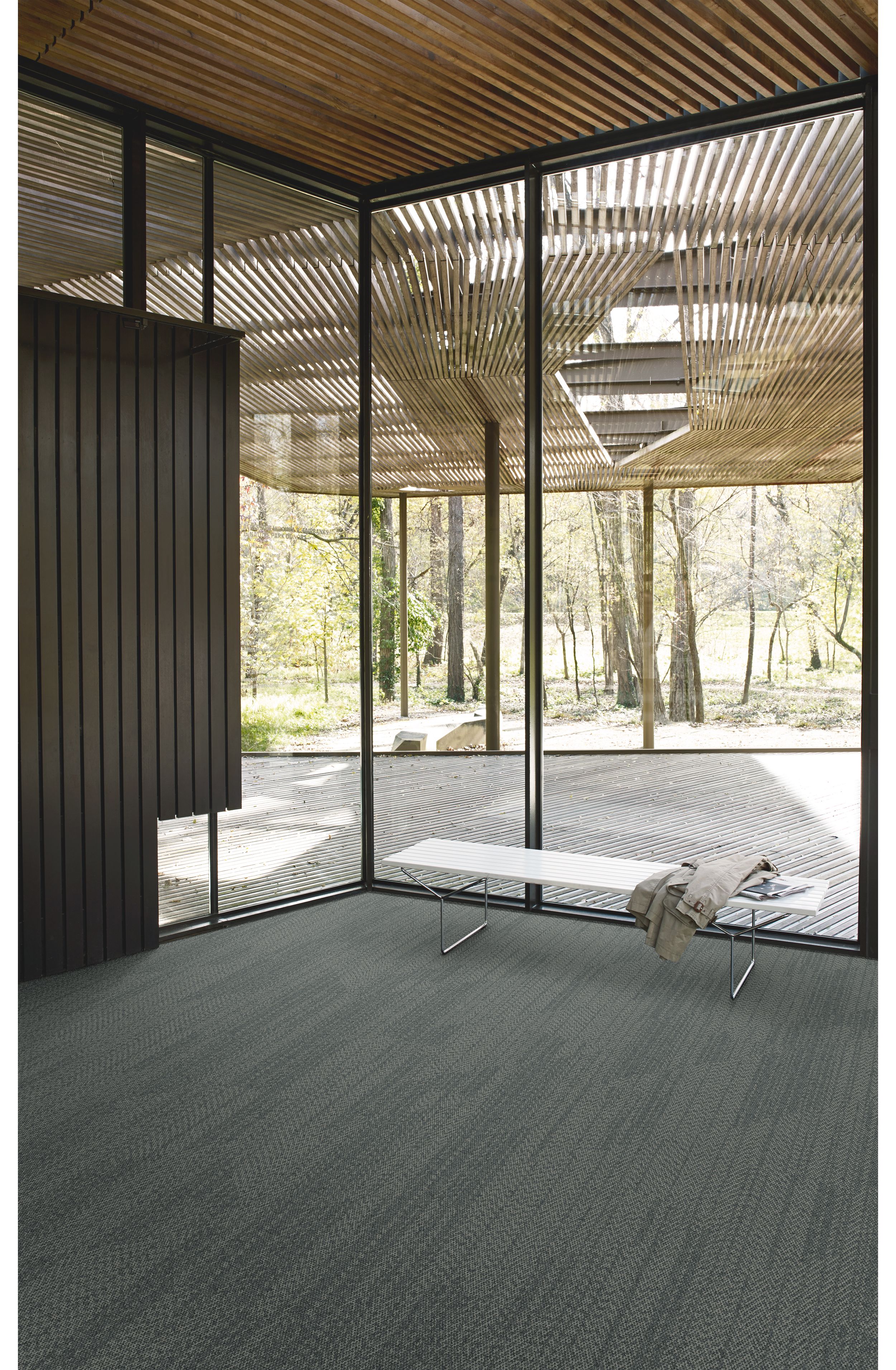 Interface Open Air 408 plank carpet tile in corner space with jacket draped over small white bench and wood slat ceiling image number 4