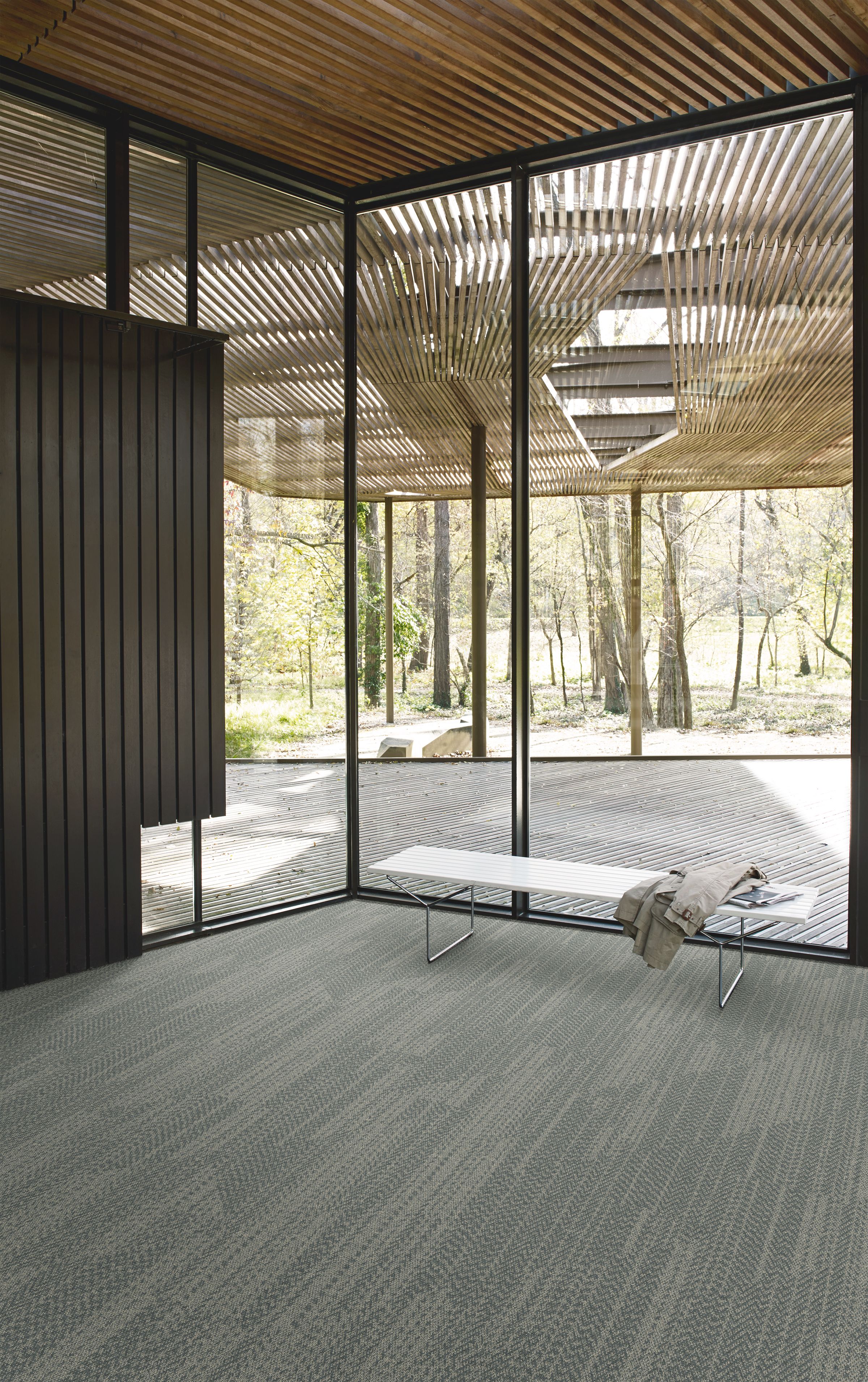 Interface Open Air 408 plank carpet tile in corner space with jacket draped over small white bench and wood slat ceiling image number 1
