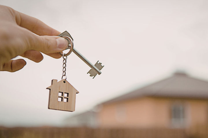 image of hand holding a key with housing graphic in the background 