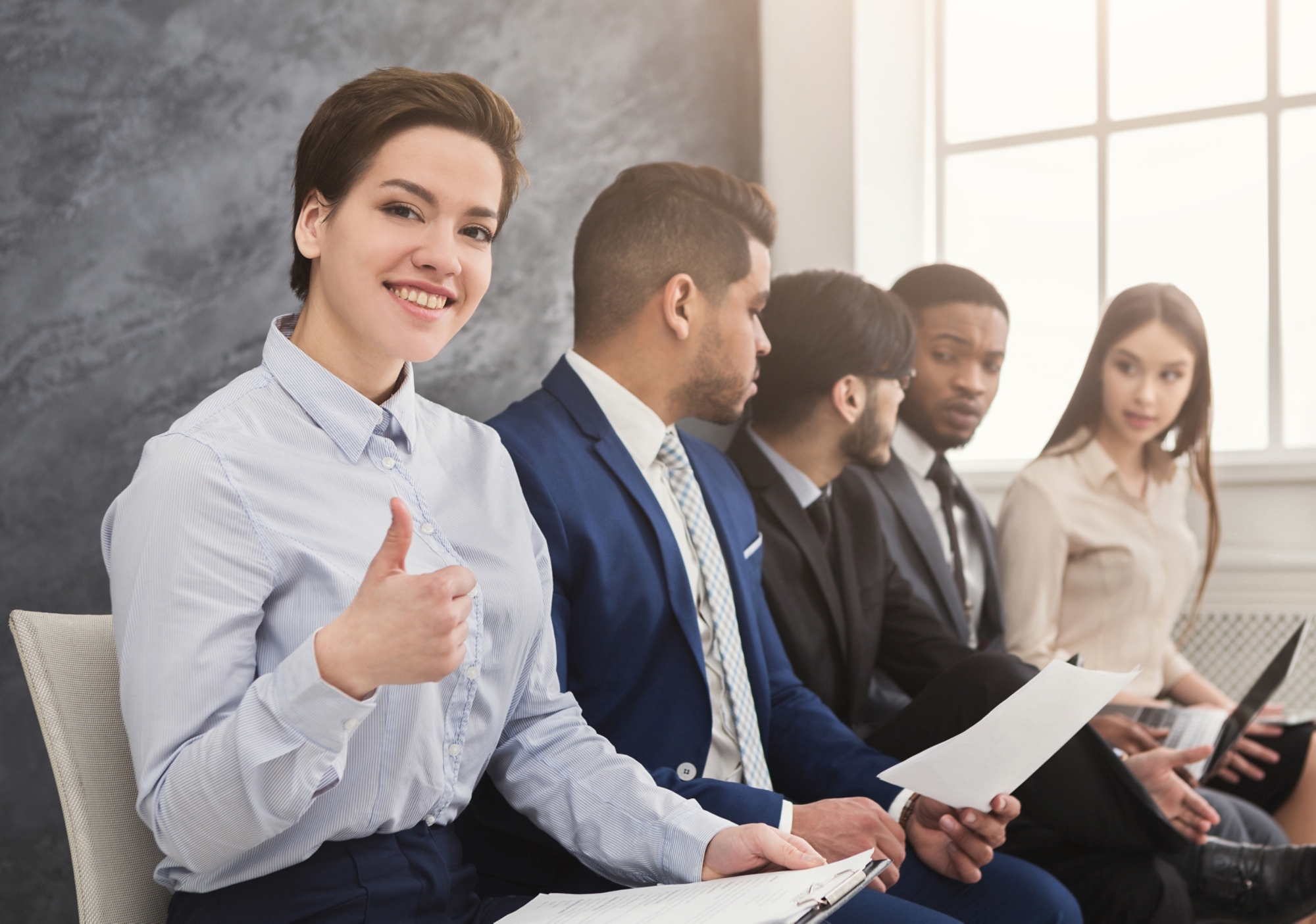 Cheerful woman showing thumb up, multiethnic people waiting in queue. preparing for job interview and reading cv, copy space