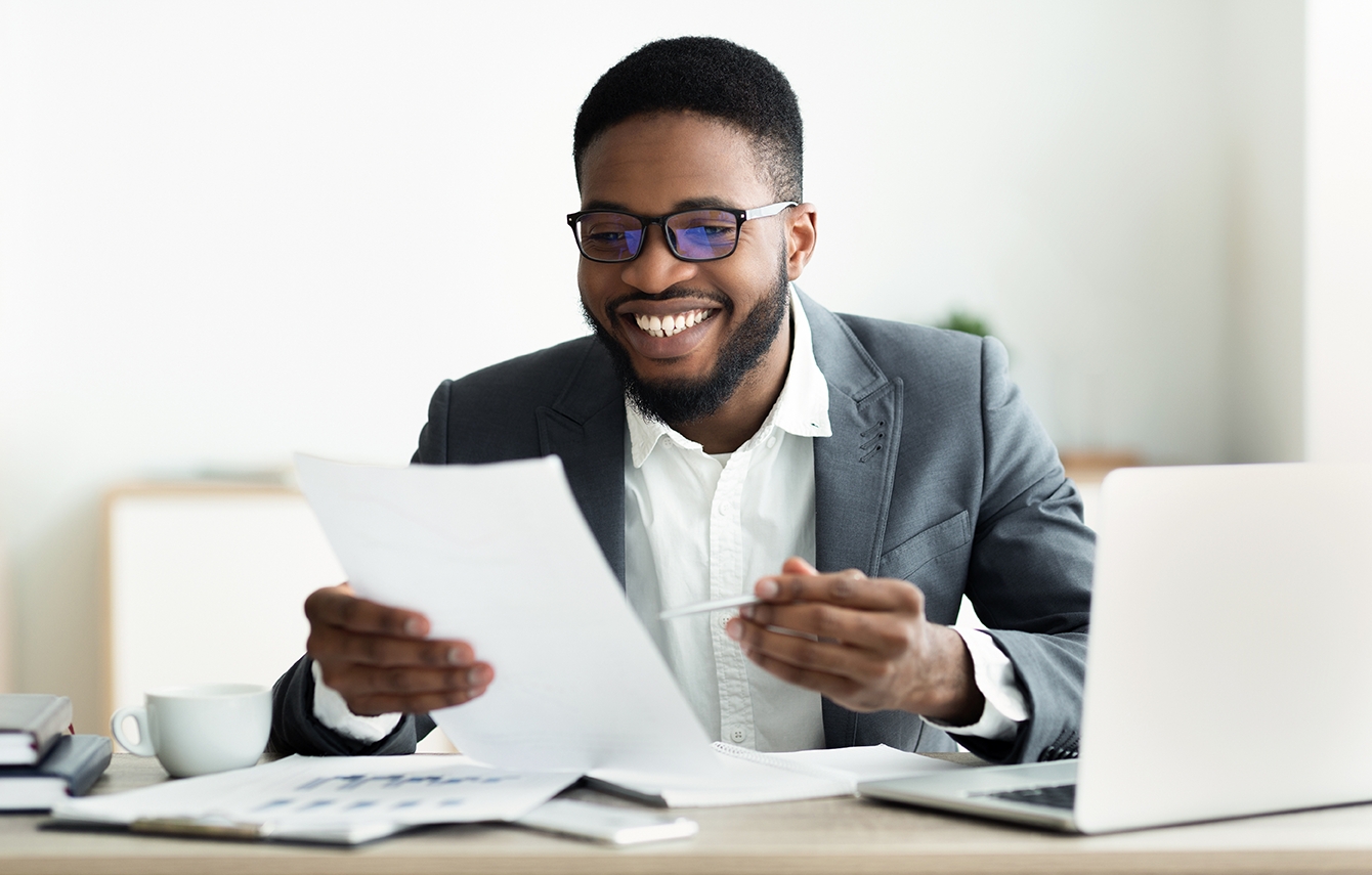 Smiling black businessman checking reports in modern office, satisfied by results of his company, copy space