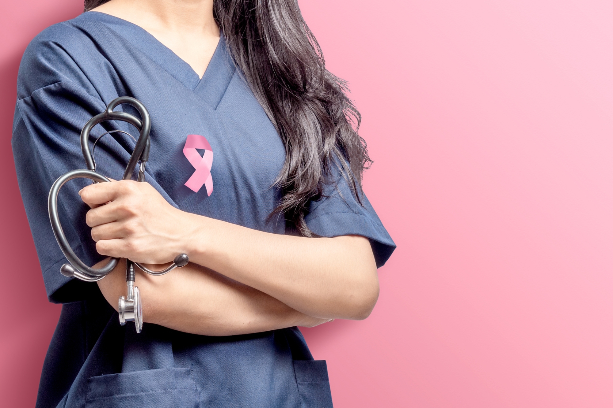 Woman doctor holding a stethoscope on her hands with pink ribbon over pink background. Breast cancer awareness