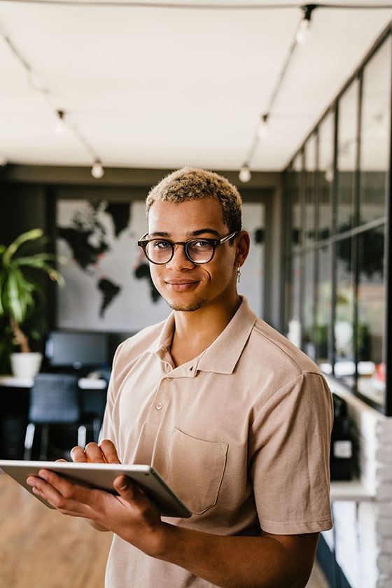 Young smiling african man in casual wear working on digital tablet while standing in modern office