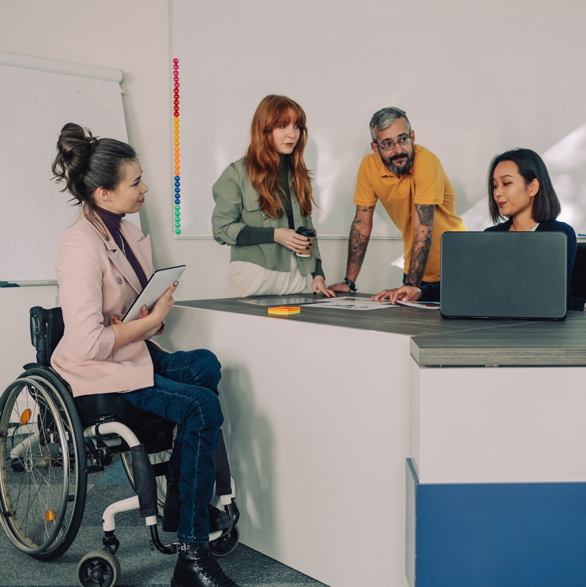 A businesswoman who uses a wheelchair is having meeting with a multicultural team. Businesspeople having meeting with a japanese female boss at office and discussing financial report. Leadership.