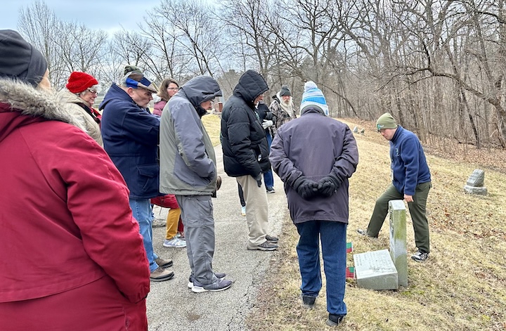 Group of people gathers around a grave marker while guide talks to them