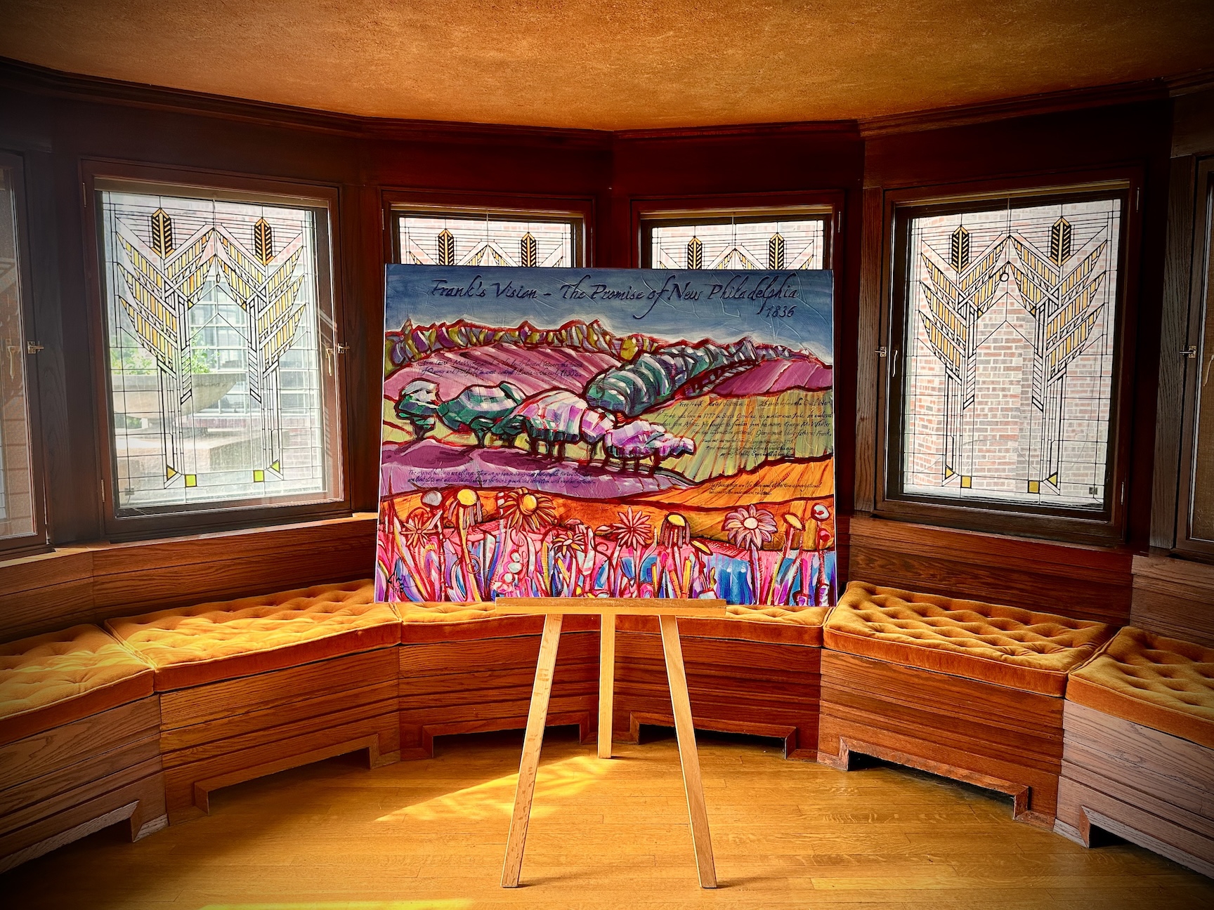 A painting of a flower-covered hillside sits on an easel in front of stained glass windows.