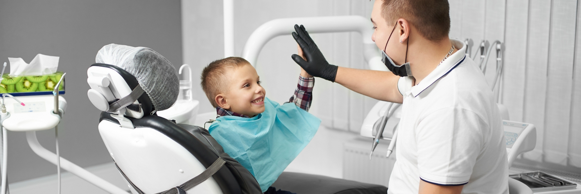 A child is happy after dental treatment and giving high-five to his doctor in a modern dental clinic.