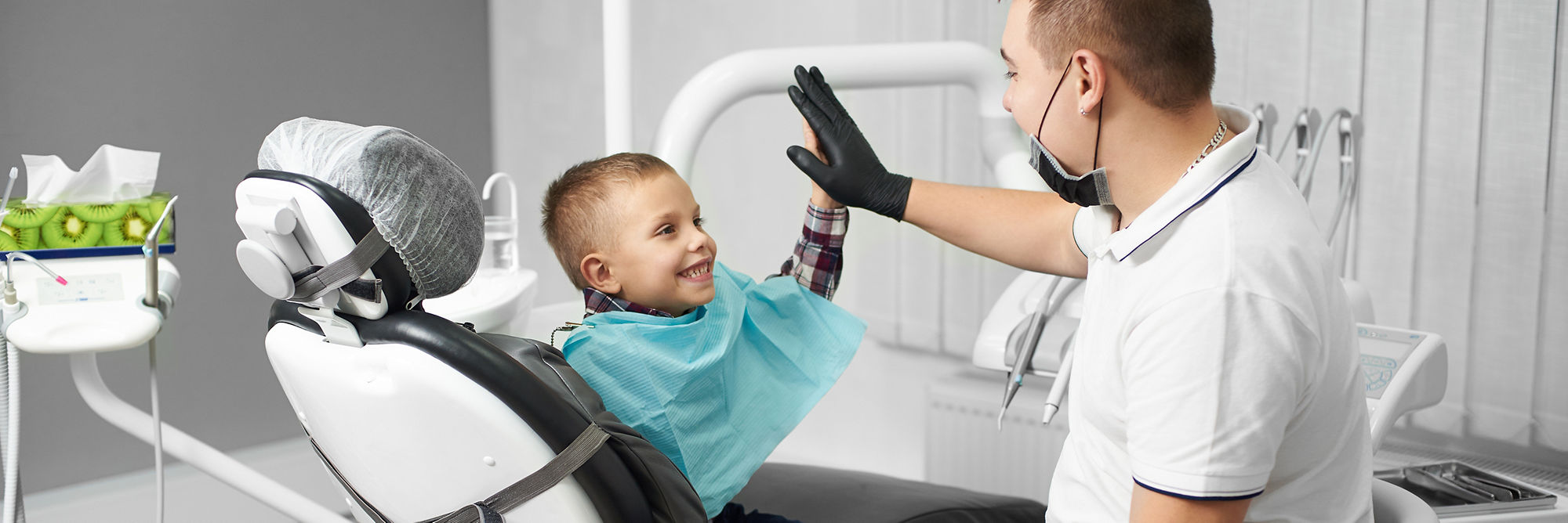 Un niño está feliz después de un tratamiento dental y choca los cinco con su médico en una clínica dental moderna.