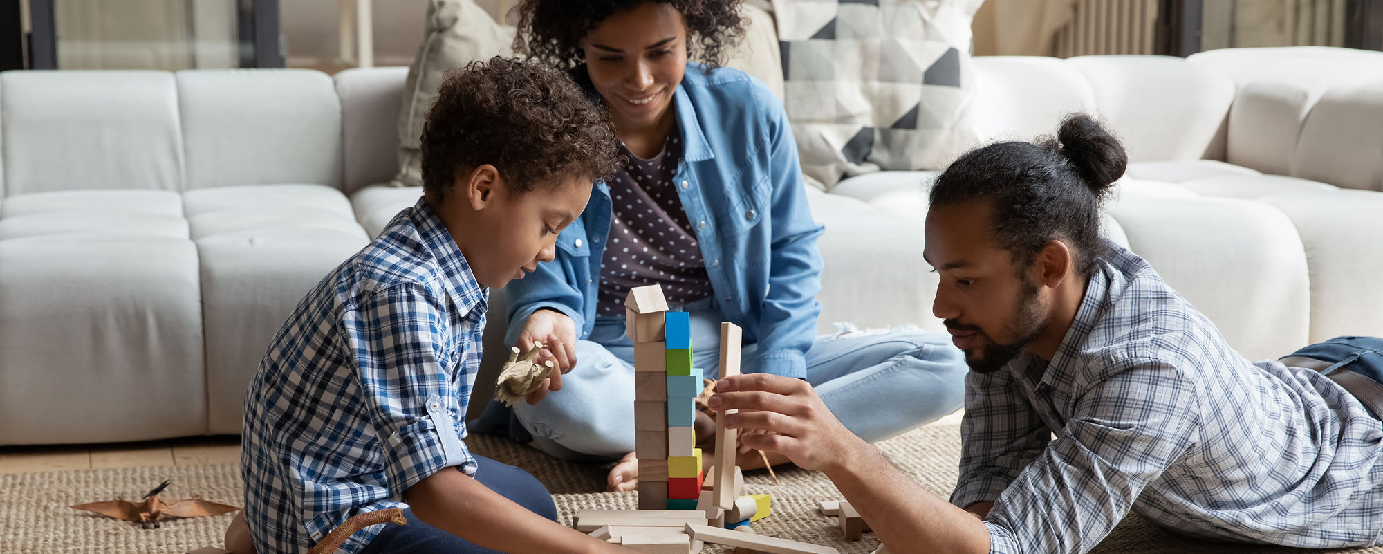 Padres afroamericanos amorosos jugando con juguetes de madera en su sala de estar con su hijo pequeño.