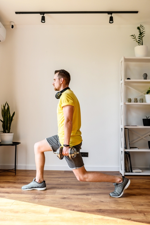 Do yourself better. Young active guy doing lower body workout at home. He doing lunges with dumbbells. The concept of a healthy lifestyle, self-discipline, sporty style