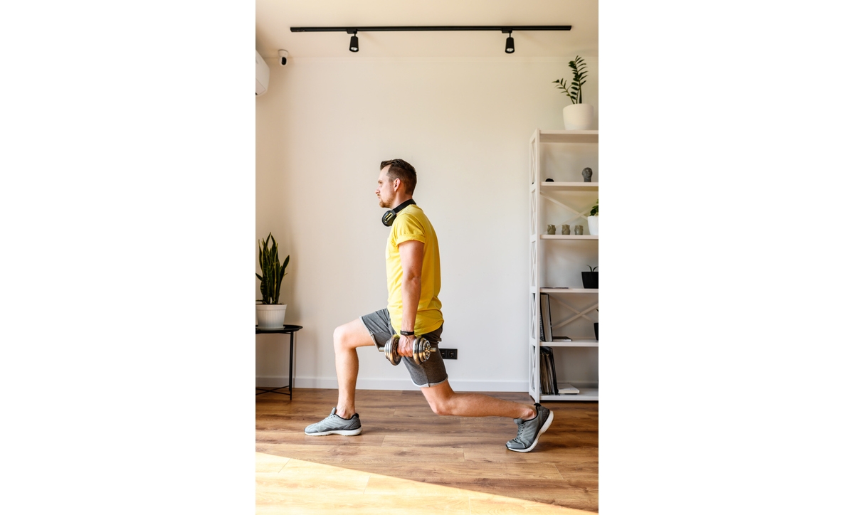 Do yourself better. Young active guy doing lower body workout at home. He doing lunges with dumbbells. The concept of a healthy lifestyle, self-discipline, sporty style