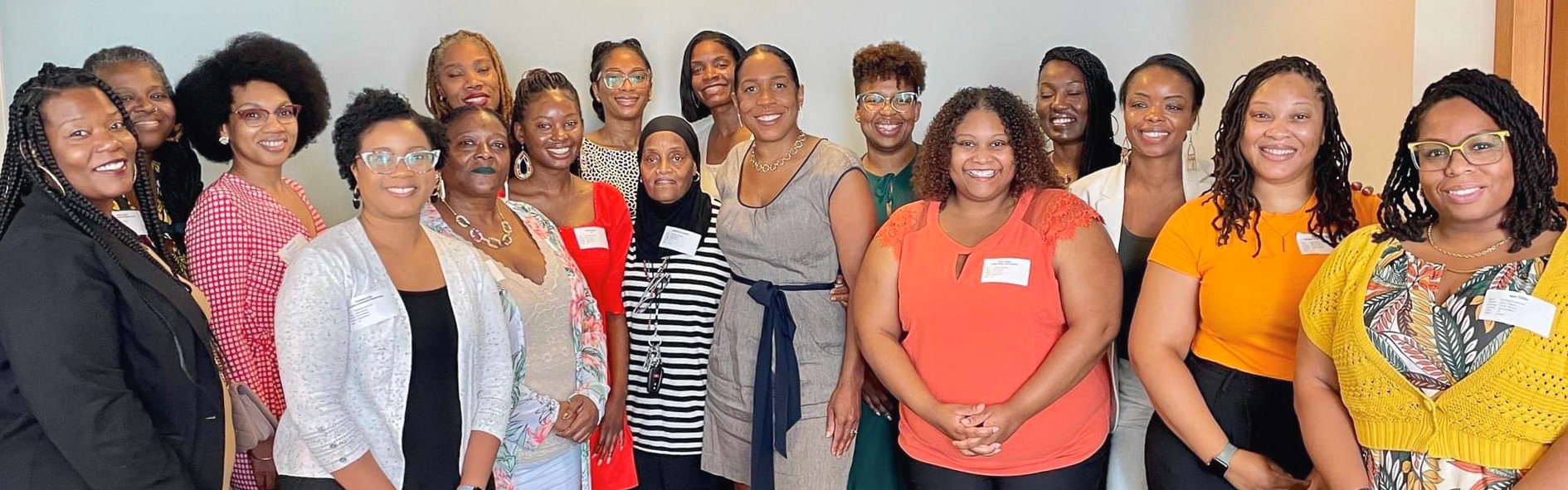 A posed group photo of Lt. Governor Stratton standing with 16 Black doulas and midwives in an office hallway, all smiling after a community conversation hosted by the Office of the Lt. Governor.