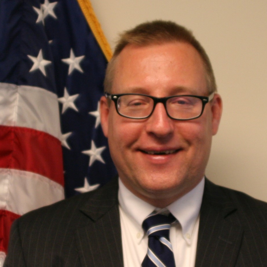 Neil Olson standing in front of an American flag.