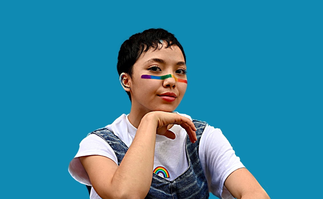 youth with short hair, rainbow face paint, seated and looking at camera