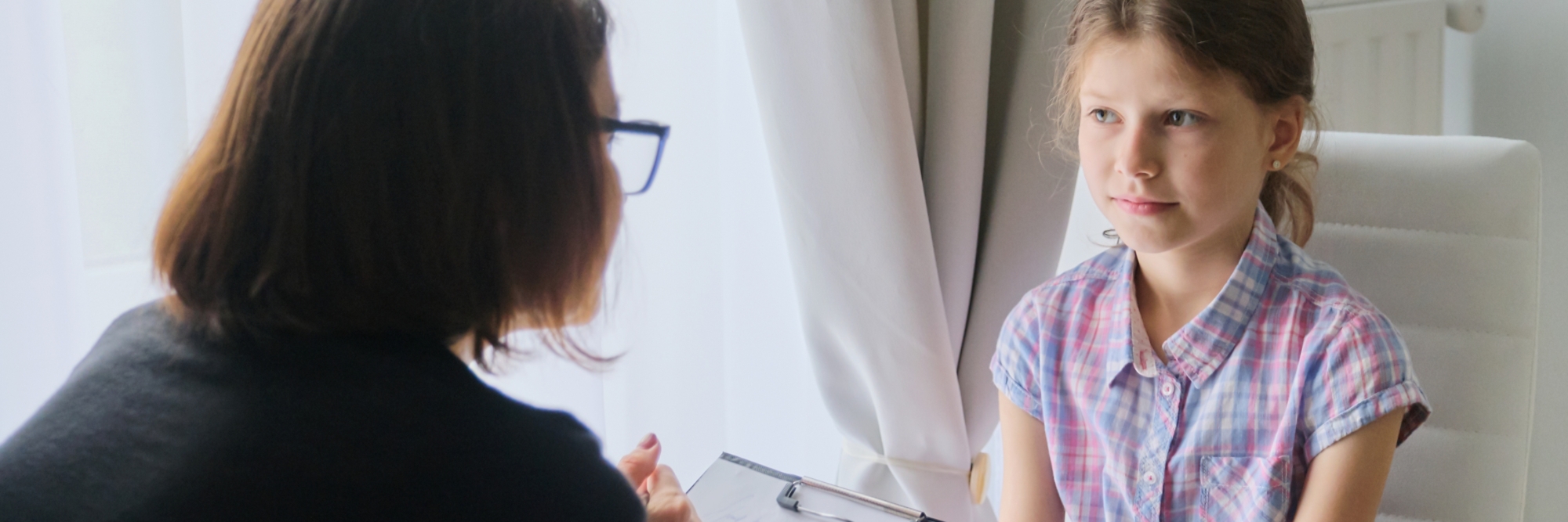A young girl sitting in a chair listening to a women who is seated across from her, holding a clipboard.