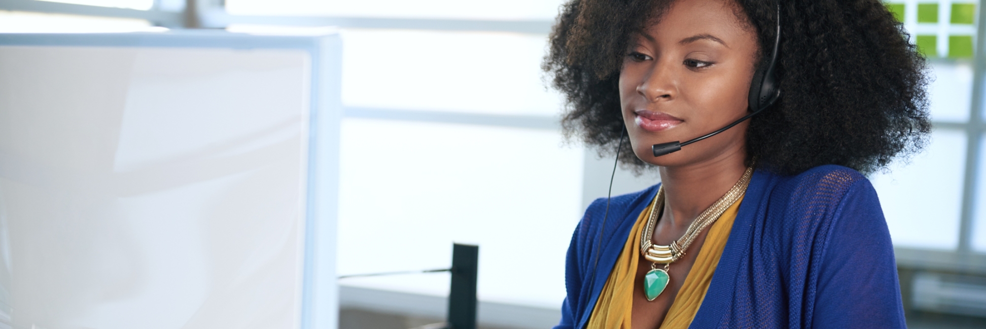 Portrait of a smiling customer service representative with an afro at the computer using headset