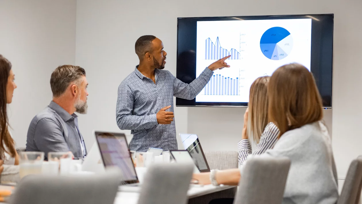  Business professional presenting data charts and graphs to colleagues in modern conference room meeting.