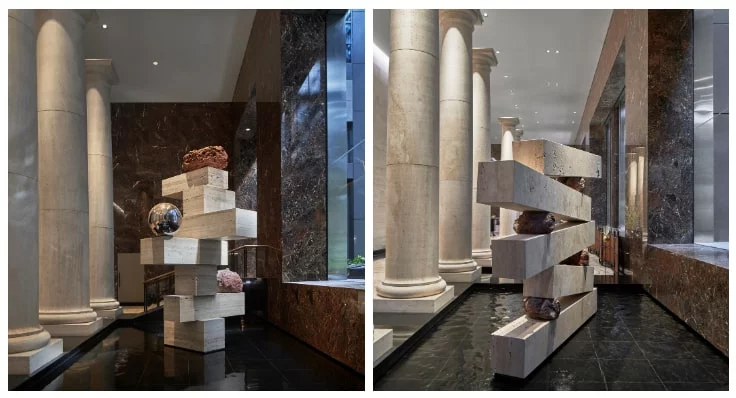Interior view of a grand lobby with large classical columns lining one side and dark polished stone walls.