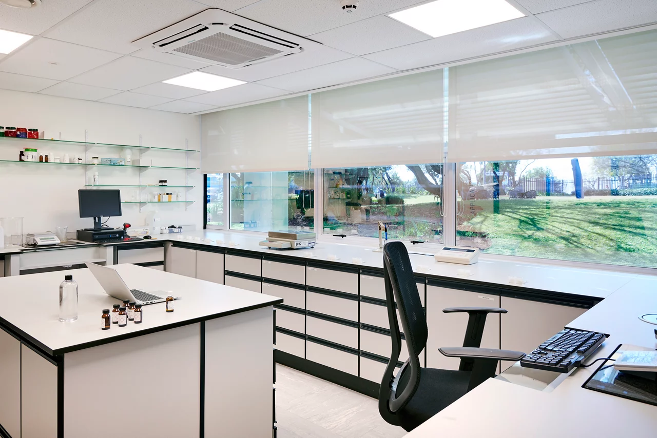 Modern laboratory with white counters, glass shelves, computers, and large windows overlooking a grassy outdoor area.