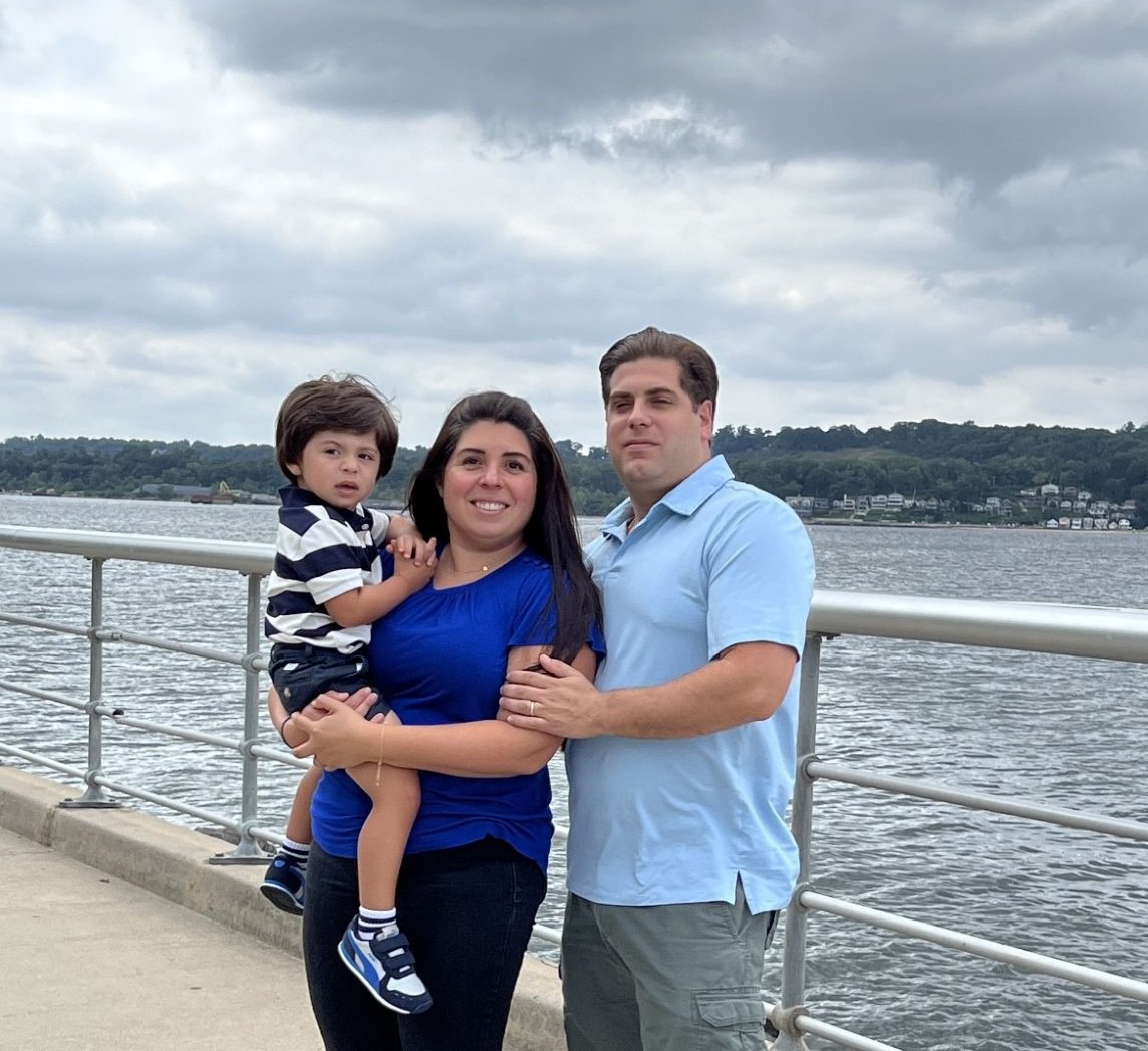 a family of 3 people standing at river front.