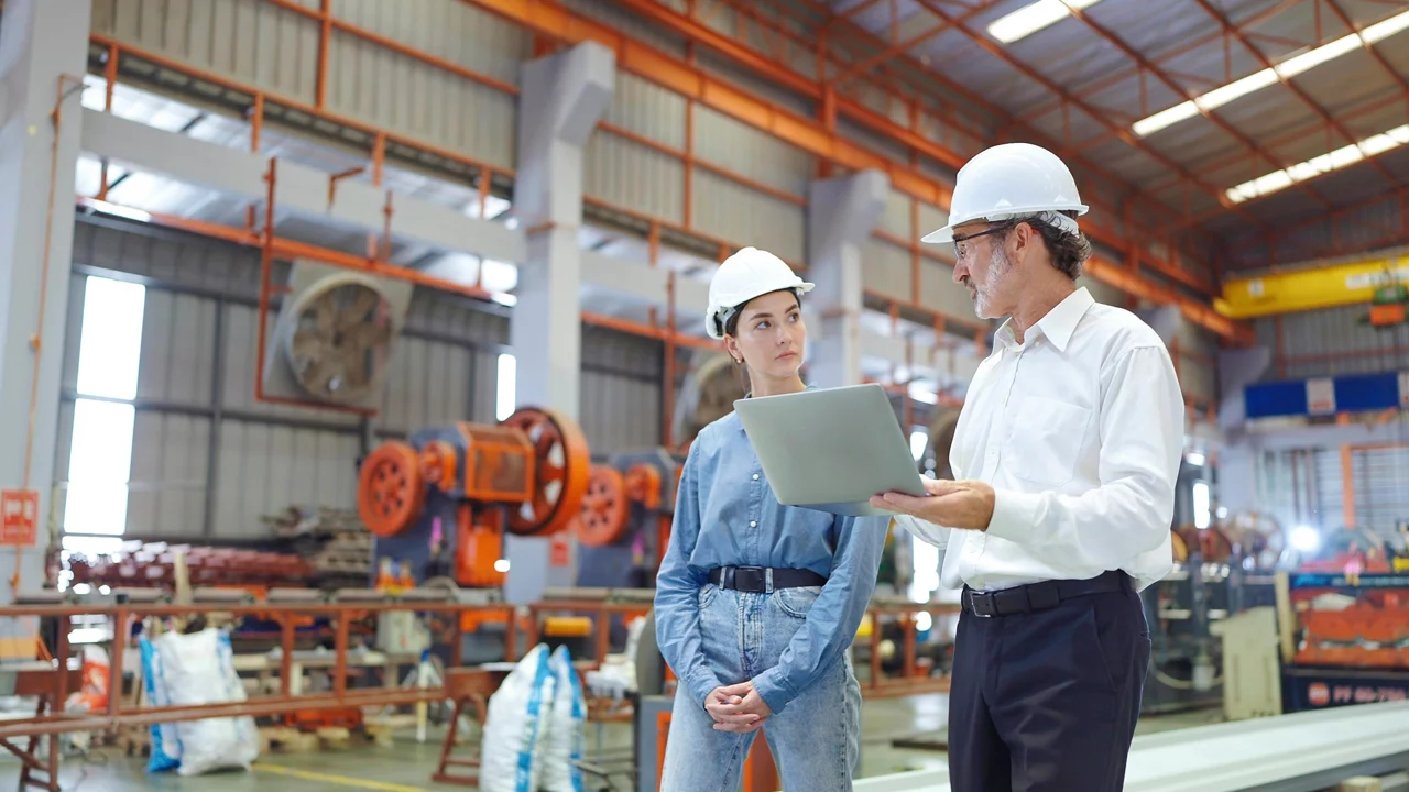 Two professional engineer man and woman manager leader wearing helmet and holding laptop walking in factory talking and discussing for work