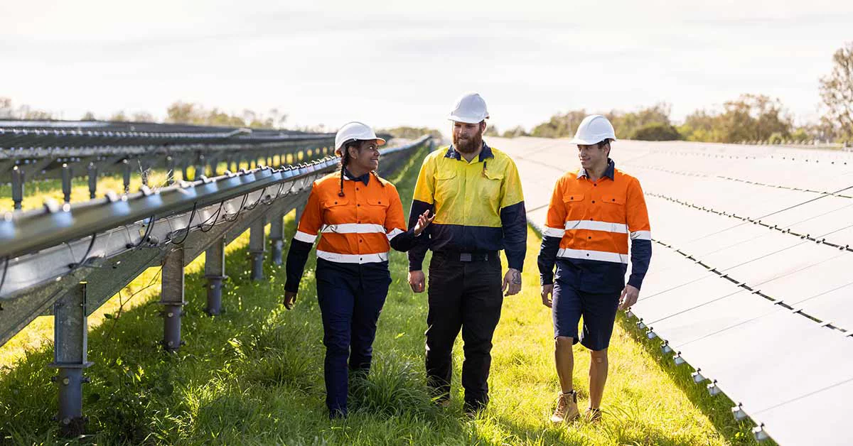 Three men in orange shirts and hard hats walking through a solar farm